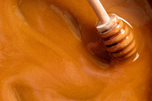 A close-up of honey with a wooden dipper swirling through it.